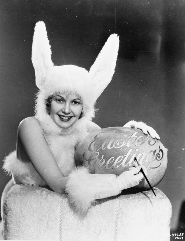 A woman wearing a rabbit outfit is writing ‘Easter Greetings’ on a large easter egg, circa 1937. Egg murder?